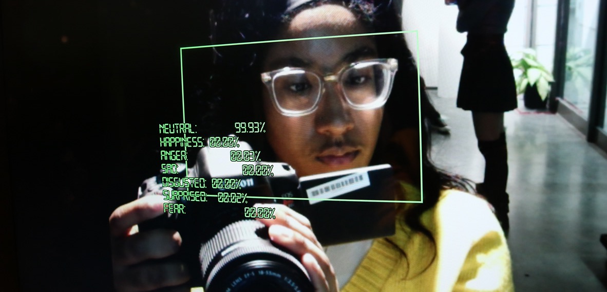 A person wearing glasses and holding a camera is framed by a green rectangle with stats of emotional percentages.