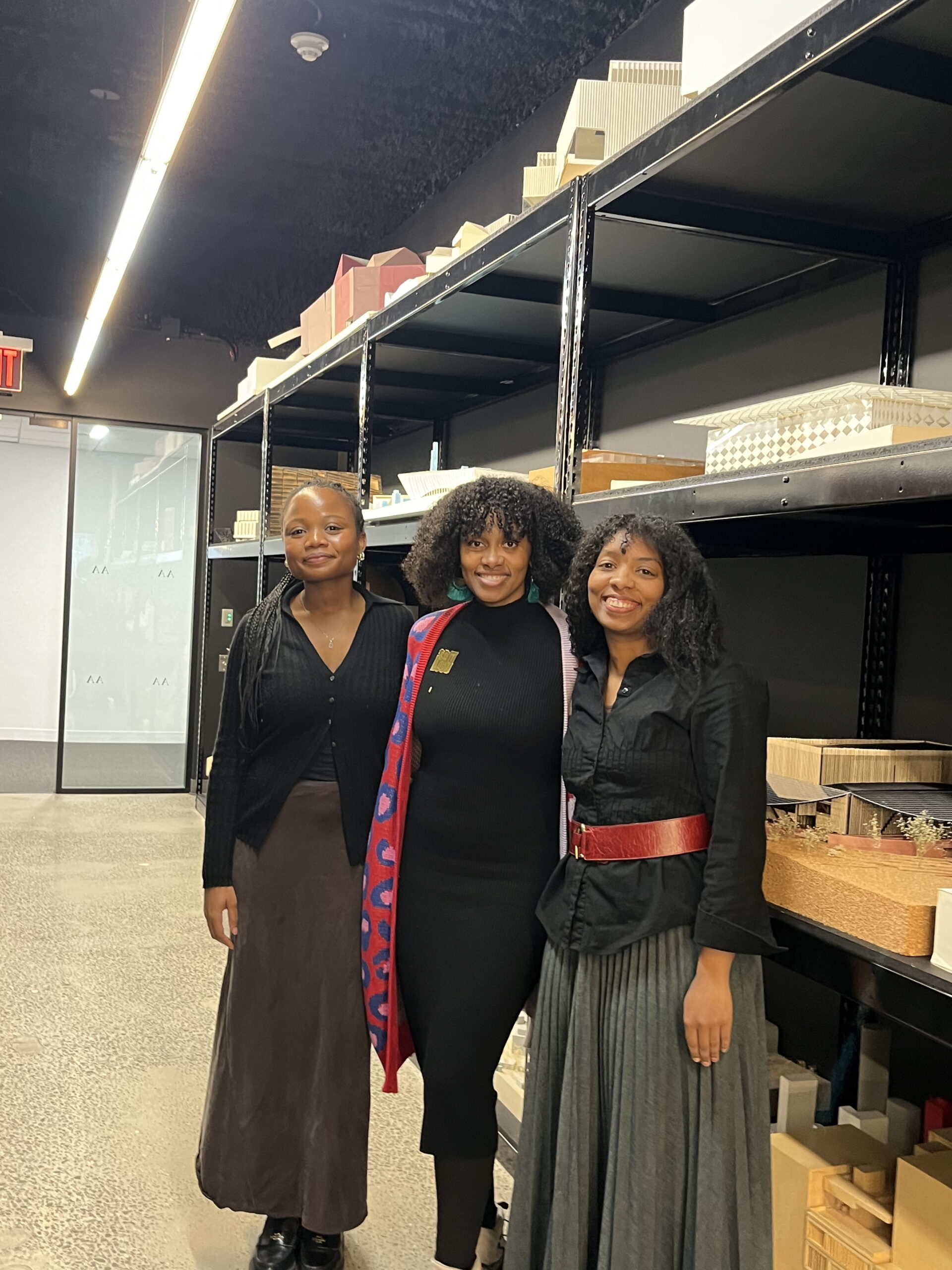 Alumna Catherine Chattergoon stands in a group photo taken from the side with two colleagues in front of large shelves filled with building models.