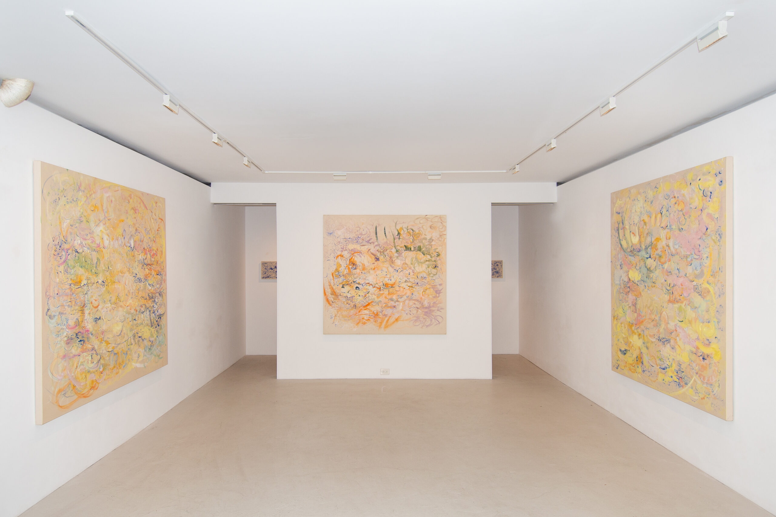 Three large abstract paintings featuring light orange, yellow, green, blue, purple, and yellow natural shapes are displayed in a white gallery space.