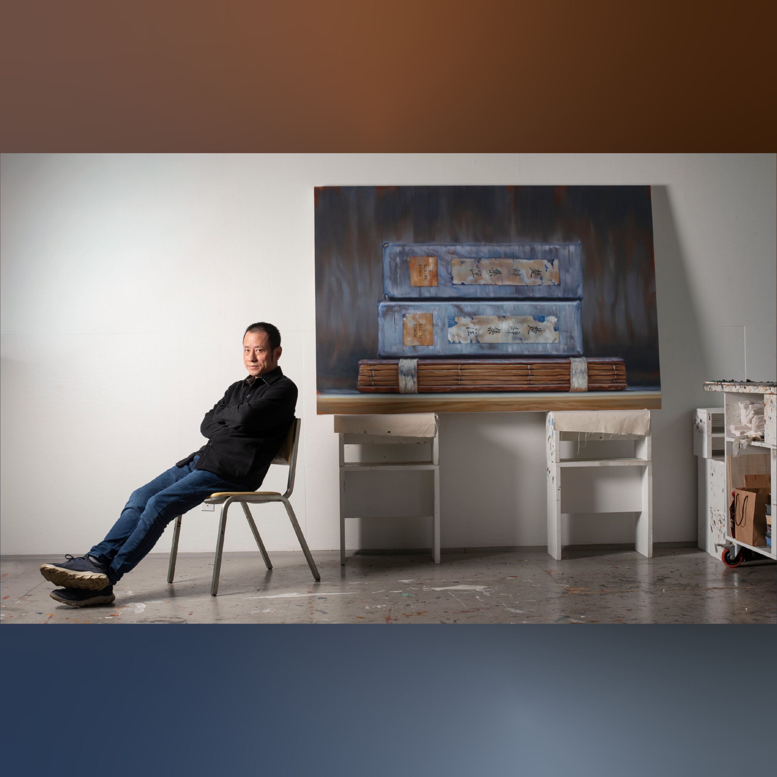 Artist Xiaoze Xie seated in his studio beside a large painting.