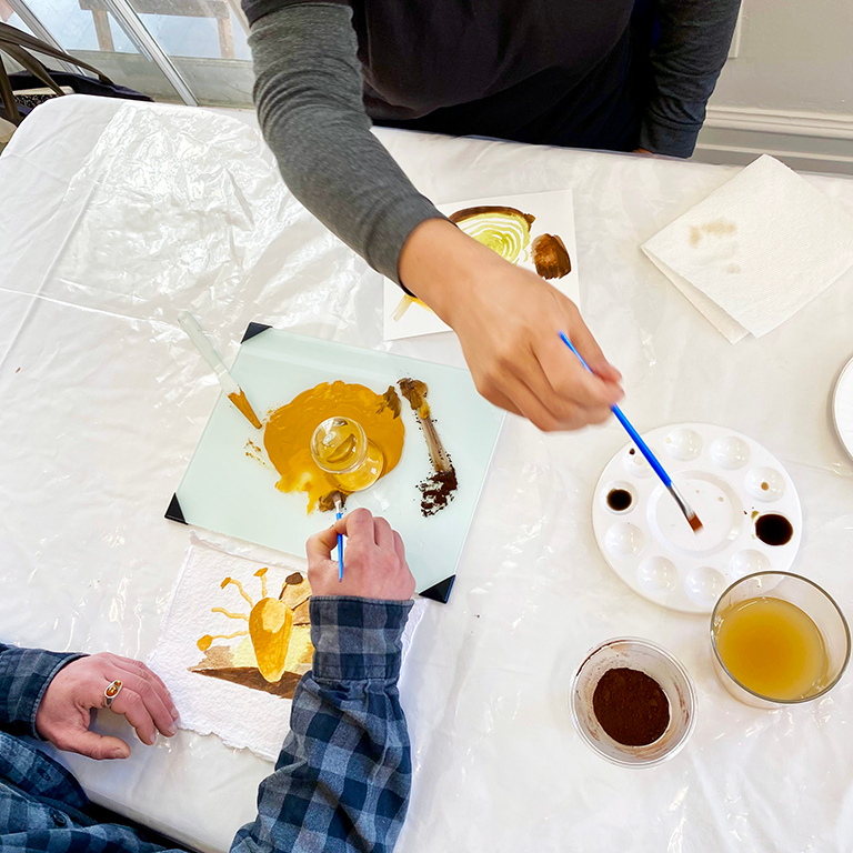 people painting with natural pigments using paintbrushes, plastic cups, palettes on a sheet of paper