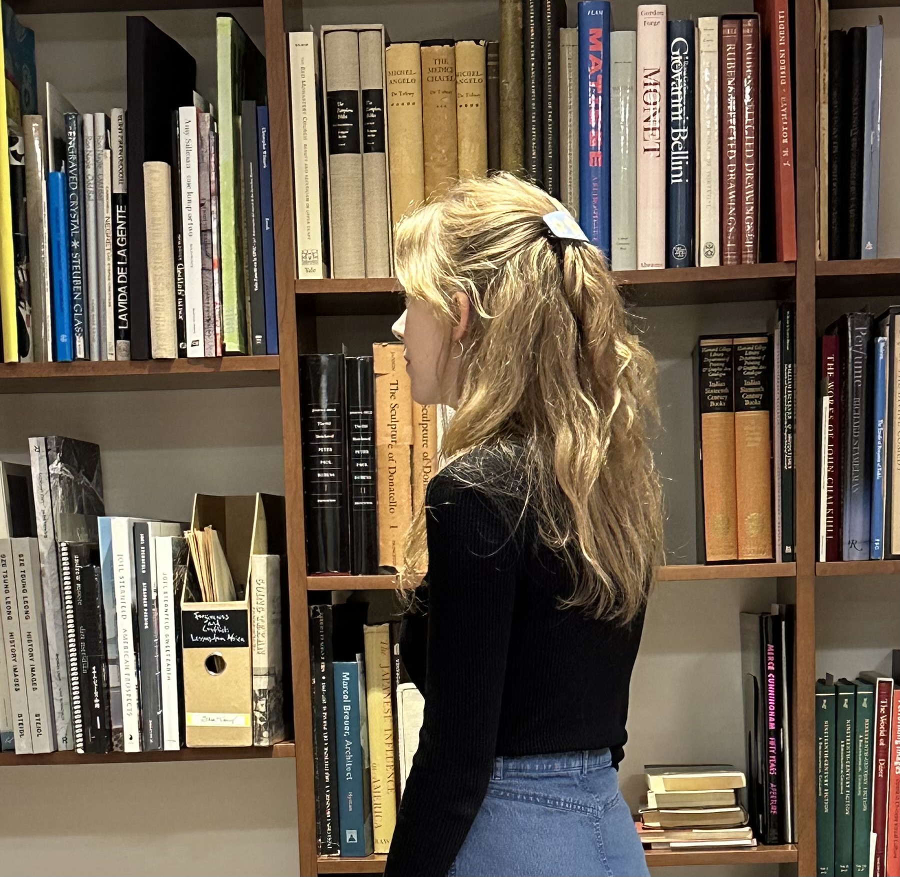A photo of alumna Hanna Pennington shows her facing a wall of books and archival material.