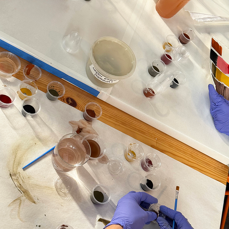people painting with natural pigments using paintbrushes, plastic cups, palettes on a sheet of paper