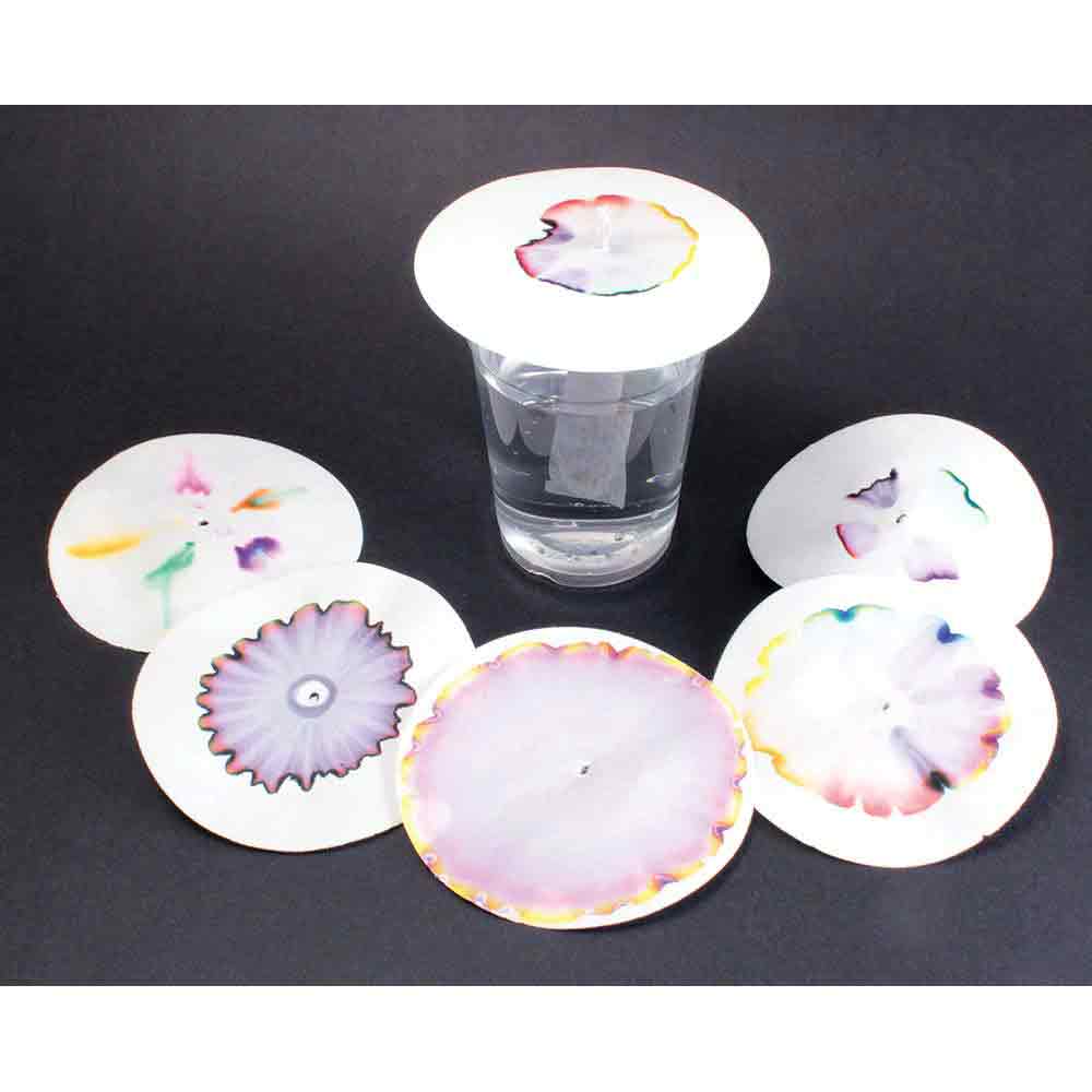 A clear glass filled with water is positioned at the center, topped with a circular lid featuring colorful floral designs. Surrounding the glass are several similar circular lids, each displaying unique watercolor patterns in various colors and shapes, resting on a dark background.
