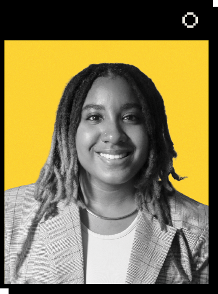 Headshot of Ananda Ray against a yellow background. Ananda is smiling and looking at the camera. She has shoulder-length locked hair and wears a light-colored shirt and a checkered blazer.