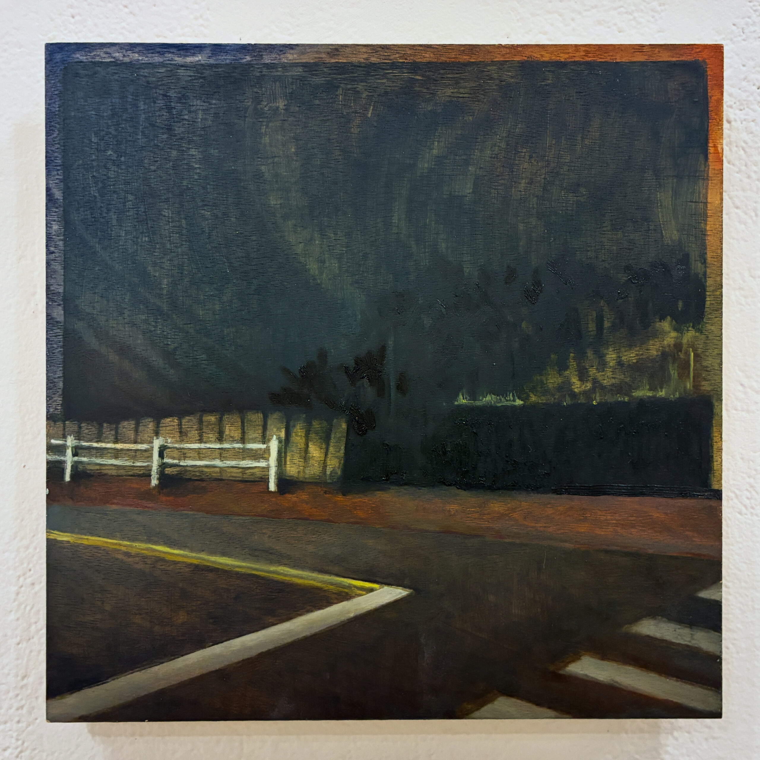 A dark, moody painting depicting a corner with a white fence and a shadowy green hedge in the background. The scene suggests nighttime or low light, with an empty road curving from the foreground. Sparse vegetation can be seen, and the atmosphere evokes a sense of quiet stillness. The colors used are predominantly dark with subtle highlights.