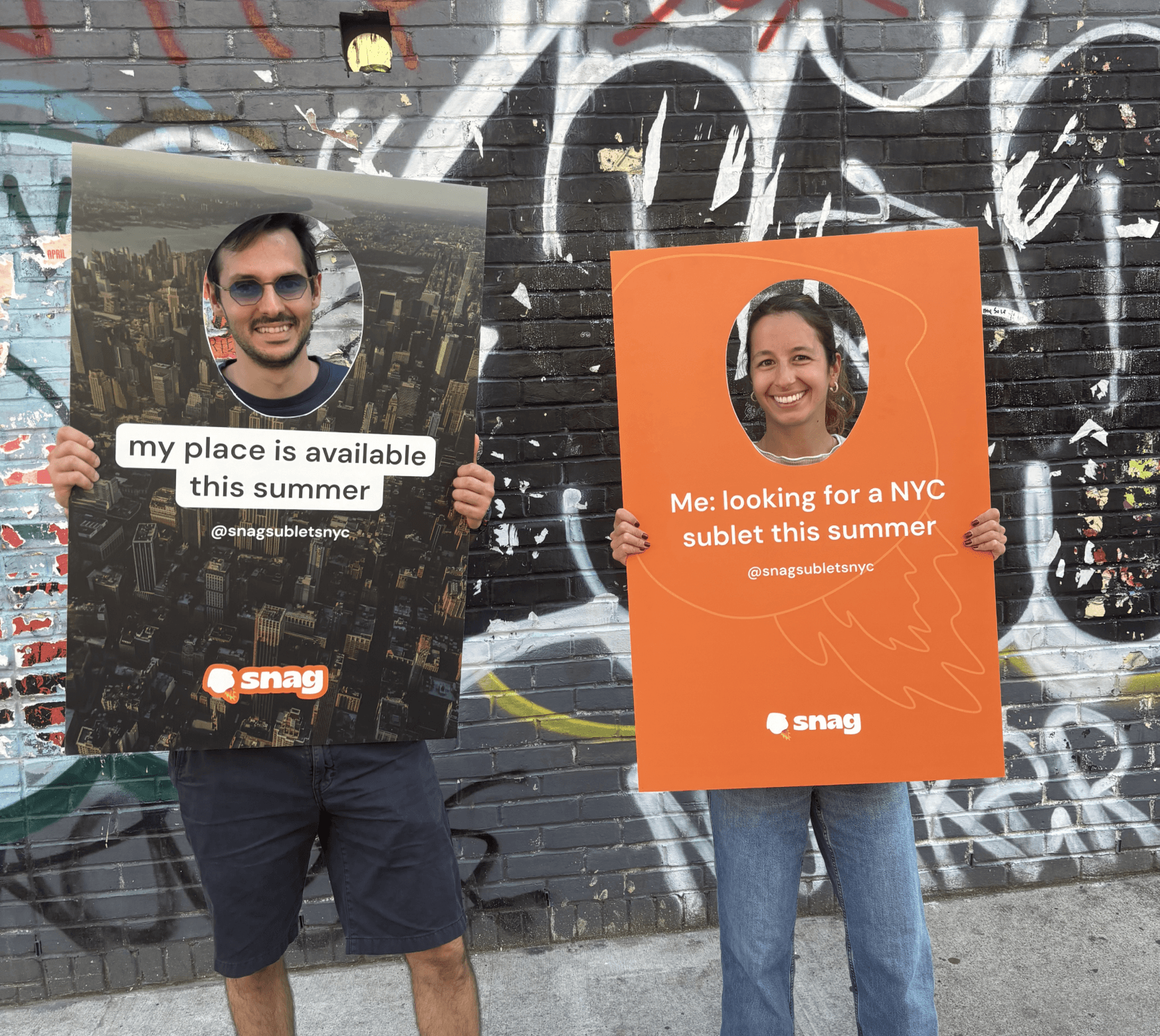 Two people stand in front of a colorful, graffiti-covered wall, holding large cardboard signs. One sign features an image of a city skyline with the text "my place is available this summer," while the other sign is orange with the message "Me: looking for a NYC sublet this summer." Both signs include the handle "@snagsubletsnyc." The individuals are smiling and engaged in a friendly interaction.