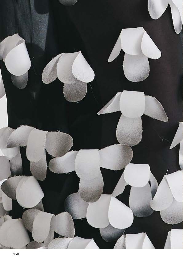 A close-up of a textured fabric featuring a pattern of overlapping white and gray petal-like shapes on a dark background. The shapes vary slightly in size and arrangement, creating a visually interesting design. The image focuses on the details and layering of the fabric.
