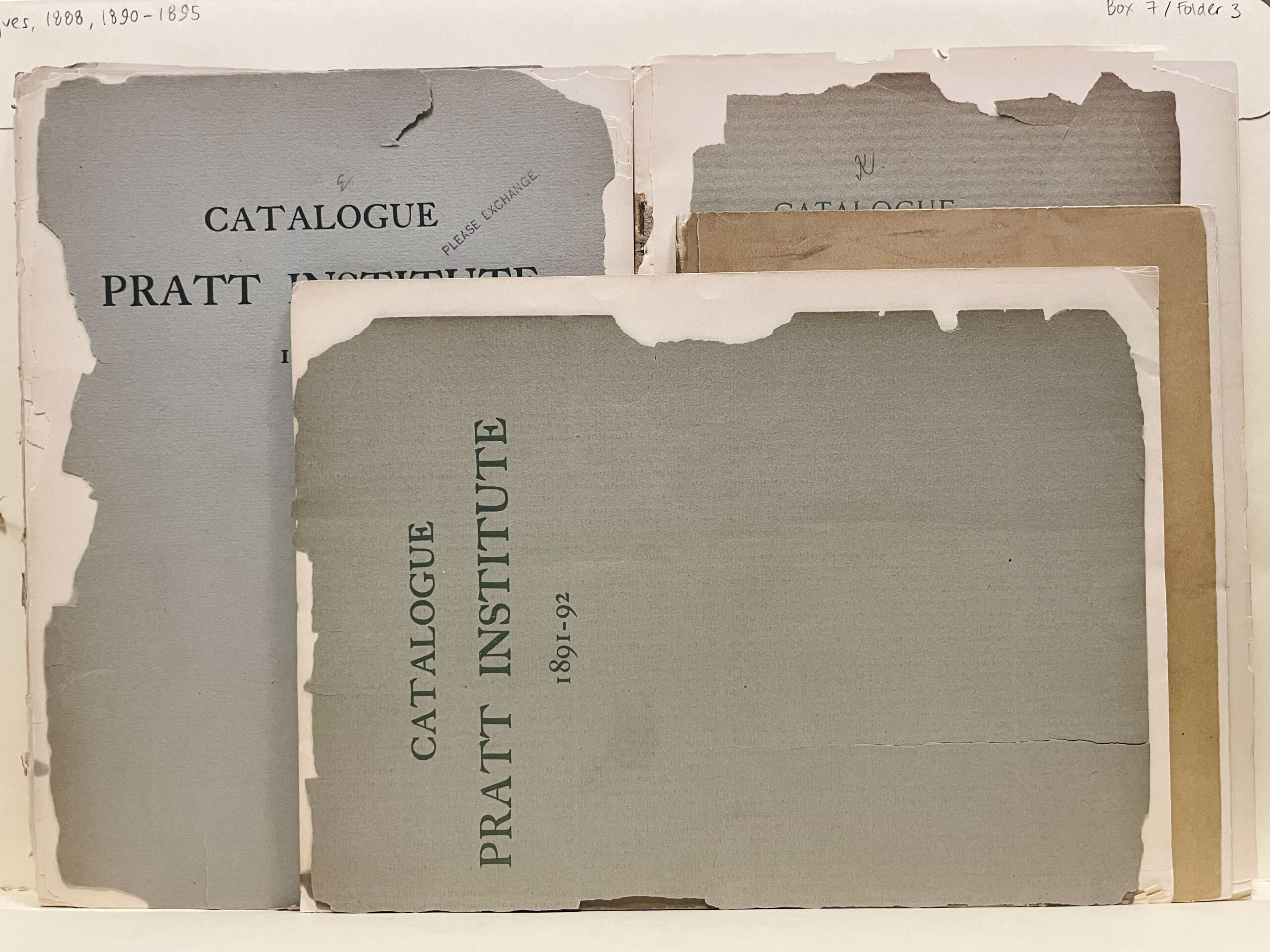 A collection of aging catalogues from the Pratt Institute, stacked and slightly overlapping. The catalogues vary in size and color, primarily featuring muted hues of gray with some fading and tearing along the edges. Text on the covers includes "CATALOGUE" and "PRATT INSTITUTE," along with respective years, such as "1891-92." The background is a light surface, and there are remnants of original bindings visible.