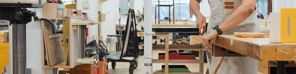 A person is cutting a piece of wood on a workbench in a woodworking shop.