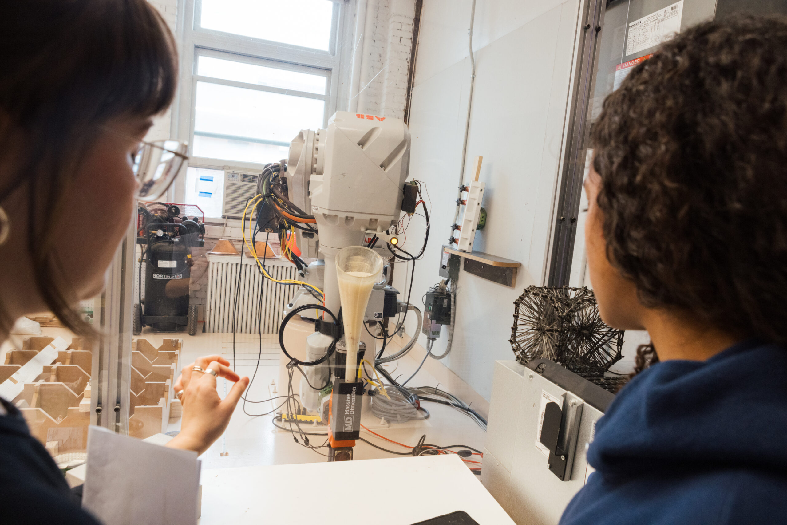 Two people observe a robotic arm operating in a workshop.