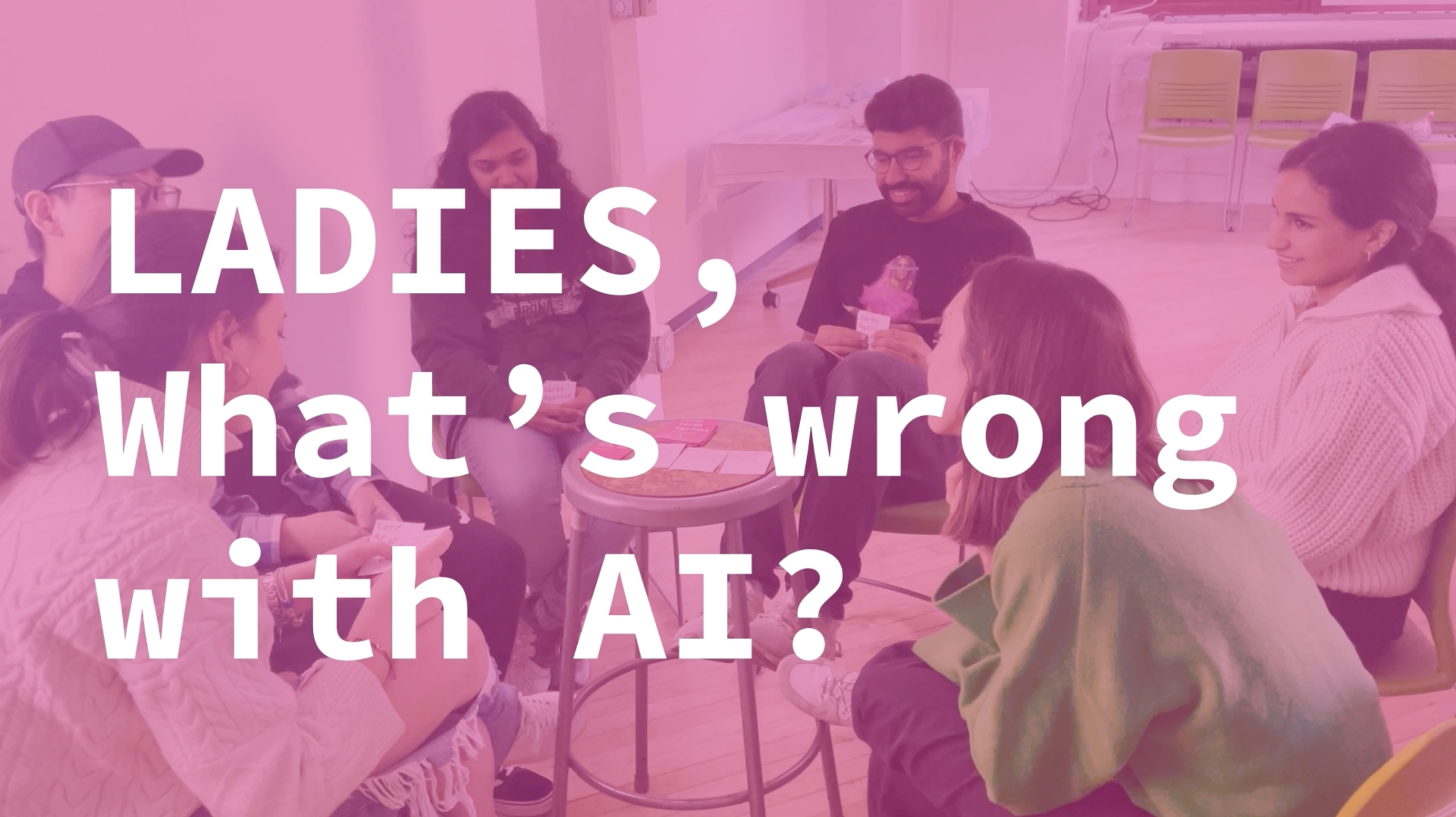 A group of people is seated in a circle on a wooden floor, engaged in discussion. They hold cards and appear to be brainstorming or sharing ideas, with a small table in the center. The background features colorful chairs and soft lighting. Text overlay reads, "LADIES, What’s wrong with AI?"