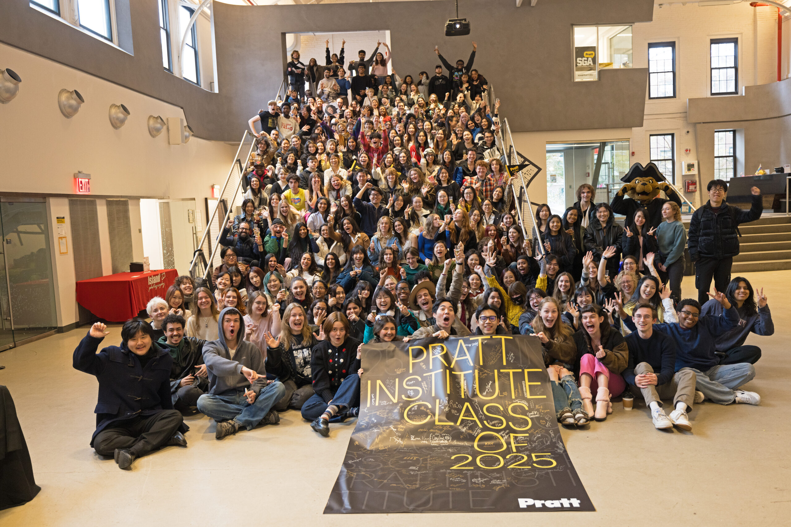 large gathering of graduating students sitting on stairs holding a banner