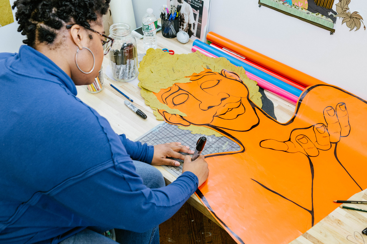 Devin Alexander in her studio working on a drawing. The drawing is a cutout that is in the shape of a person.