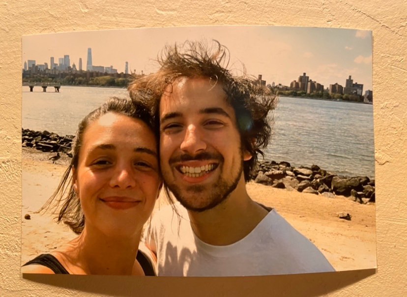 Frances Waite and Ian Valentine on a rocky beach with water and a city behind them.